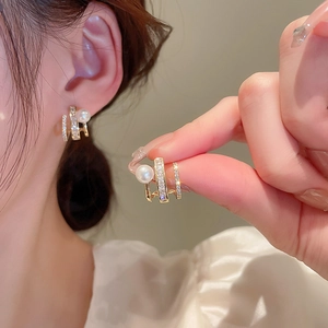 Close-up of gold layered C-shape earrings with white pearl and sparkling zircon details