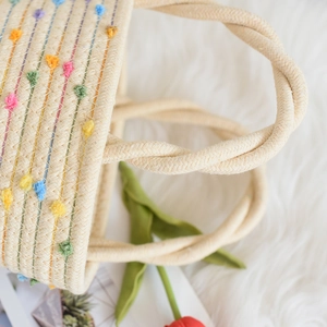Detail einer beigen Tasche aus Baumwollkordel mit bunten Pompons und gedrehtem Griff