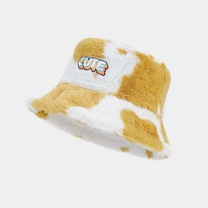 Détail d'un bob en peluche imprimé vache jaune avec un écusson brodé CUTE
