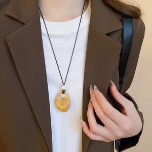 Detail of amber resin oval pendant on dark brown cord with white bead accent