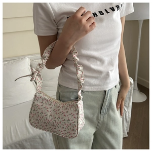 Detail of floral underarm bag with ruffled strap and bow held by model in casual setting
