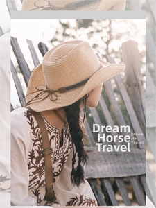 Detail of light brown woven straw cowboy hat with dark band and side bow on wooden fence
