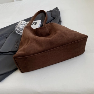 Detail of brown suede tote bag with smooth leather handles near a blazer and a book