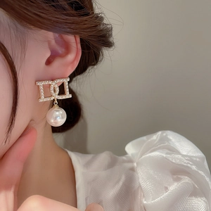 Detail of elegant gold-tone earrings with faux pearl D-letter design on a model