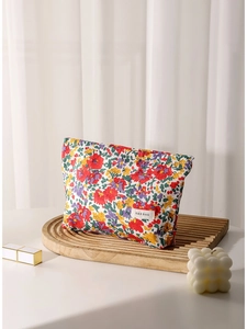 Floral fabric makeup bag with red and yellow flowers on a wooden tray for travel