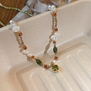 Detailed close-up of Baroque pearl necklace with green emerald-cut gemstone pendant