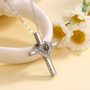 Silver cross necklace with heart detail and projection stone on warm floral background