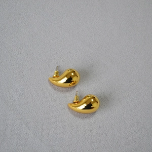 Close-up of golden teardrop earrings with mirror-polished finish on grey texture