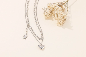 Detail of silver double-layer chain with heart and girl pendants on beige background