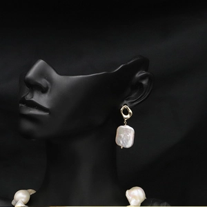 Detailed view of baroque pearl earrings with golden accents on a black background