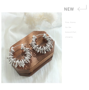 Detailed view of silver spiral hoop earrings on a vintage octagonal wooden stand