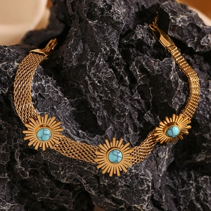 Macro detail of a 18K gold mesh bracelet with turquoise sunburst motifs on dark rock