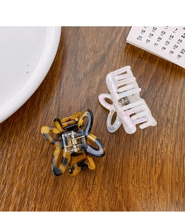 Detail view of acetate butterfly hair claws in amber and pearl white on a wooden surface