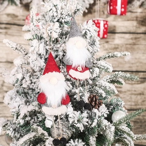 Hanging Christmas gnome plush ornaments with long legs on a snowy pine tree branch