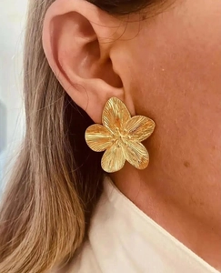 Close-up of oversized golden flower earrings featuring realistic brushed metal texture