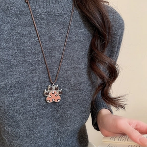 Detail shot of the pink leopard print cat paw pendant on a brown woven necklace cord