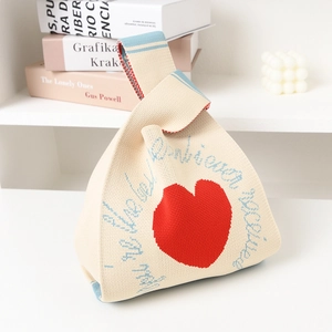Knitted tote bag with red heart pattern and blue lettering on a minimalist table