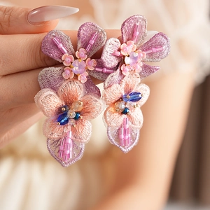 Detail of handcrafted floral earrings with vibrant purple and pink embroidery and crystals