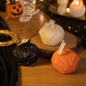 Three pumpkin-shaped scented candles in black, white, and orange on a wooden base