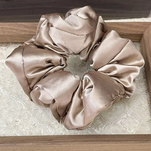 Macro detail of a champagne satin scrunchie showing smooth silky texture on a glass tray