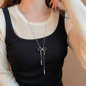 Silver bow pendant necklace with long tassel chain style worn by a female model