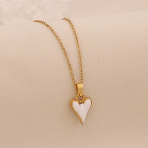 Collier en chaîne dorée avec pendentif cœur émaillé blanc sur fond clair texturé
