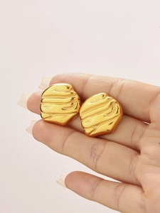 Macro view of gold plated organic ripple earrings held by hand to show the exact size