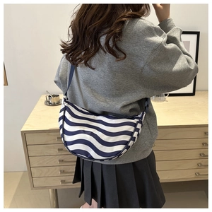 Blue and white wave pattern dumpling bag worn crossbody by a model in a casual setting