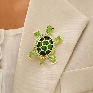 Broche tortue vintage en or avec cristaux verts sur le revers d'un tailleur beige