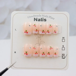 Detail of pink French press-on nails with cherry patterns and rhinestones in XS size
