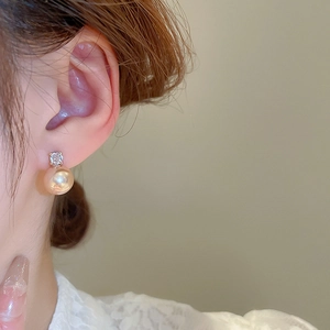 Close-up of elegant champagne pearl earrings with zircon inlay worn by a model