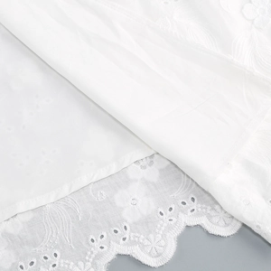 Detailed close-up of white floral hollow embroidery and scalloped lace edge on a dress