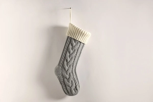 Close-up of grey knitted Christmas stocking with white fold-over cuff on plain wall