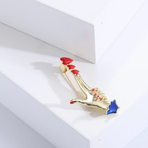 Close-up of golden hand gesture brooch with red heart and blue crown cuff detail