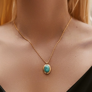 Detail van een gouden ketting met turquoise hanger gedragen om de hals