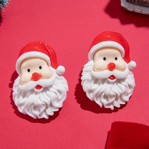 Gros plan de boucles d'oreilles Père Noël en résine avec bonnets rouges sur fond rouge
