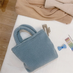 Dettaglio della borsa blu in peluche appoggiata su letto a righe e pavimento in legno