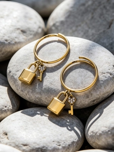 Close-up of gold stainless steel hoop earrings with crystal lock and key pendants