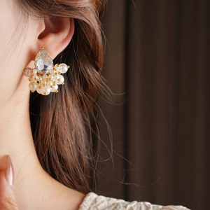 Detailed close-up of crystal teardrop earrings with white pearls on a gold base