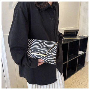 Detail of zebra print envelope clutch with golden triangle metal trim held by a model