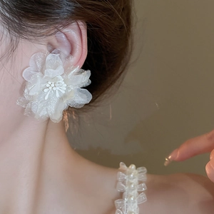 Close-up of a white oversized mesh flower earring with a pearl center on a female model