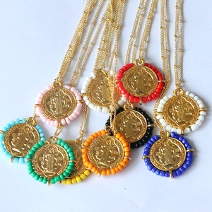 Close-up of colorful St. Benedict medal pendants with golden bead chains on white base
