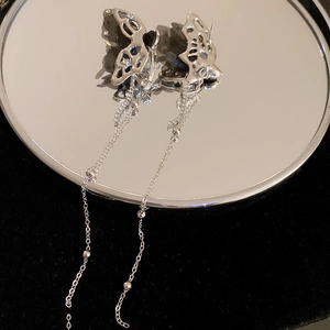 Detailed close-up of hollow butterfly earrings with long tassels on a dark surface