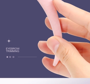 Detail of hand holding pink eyebrow trimming tool with comb on purple background