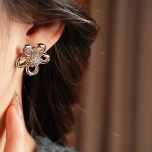 Detailed close-up of zircon hollow flower stud earrings worn on the earlobe