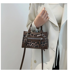 Detail of leopard print handbag with leather trim held by a model in a beige trench coat