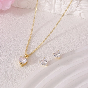 Elegant gold necklace and heart zircon earring set for women on white textured background