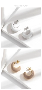 Detailed view of candy-colored C-shaped enamel earrings in white and beige finishes
