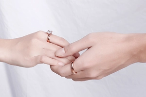 Close-up of rose gold couple rings with diamond engagement ring on a couple's hands