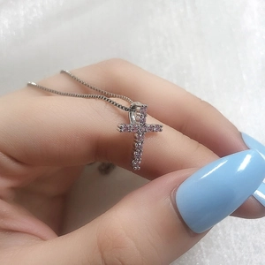 Close-up of silver cross necklace with pink zircon stones held against a white background